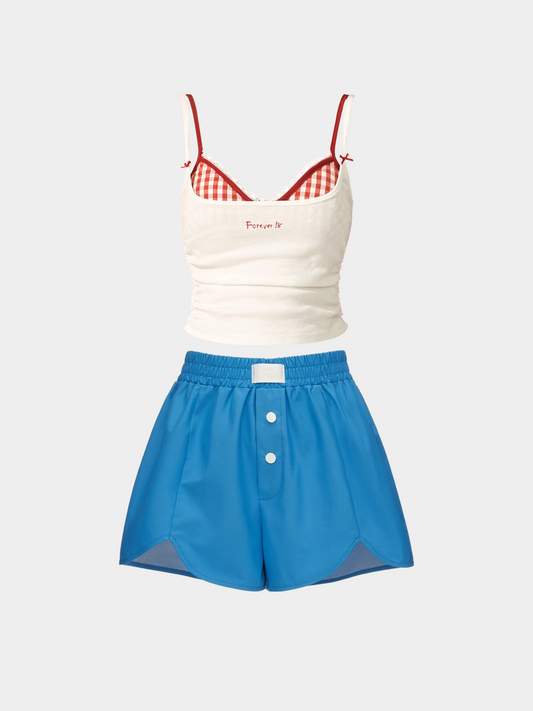 White tank top with red checkered straps and blue shorts on a light gray background