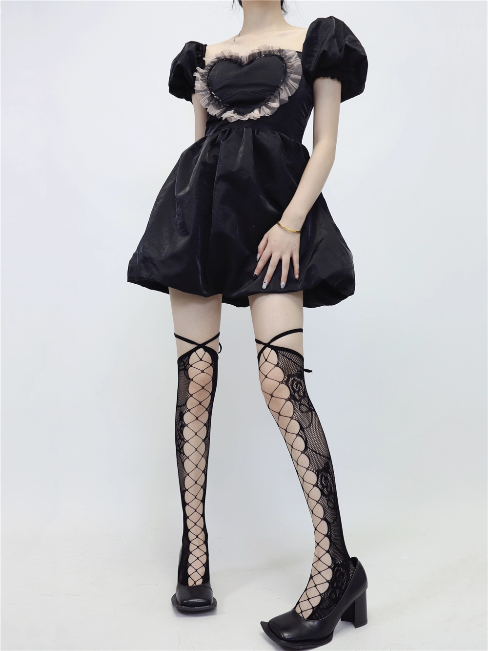 Person wearing a black dress with puffed sleeves and fishnet stockings on a white background