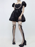 Person wearing a black dress with puffed sleeves and fishnet stockings on a white background