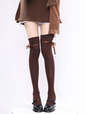 Brown knee-high socks with bow details worn over a white skirt and brown sweater on a white background.
