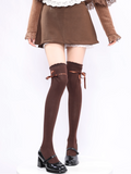 Brown knee-high socks with bow details worn with a skirt and black shoes on a white background