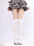 Person wearing white stockings with ruffles and a gray skirt on a light gray background