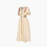 Beige dress with floral embroidery and black buttons on a white background