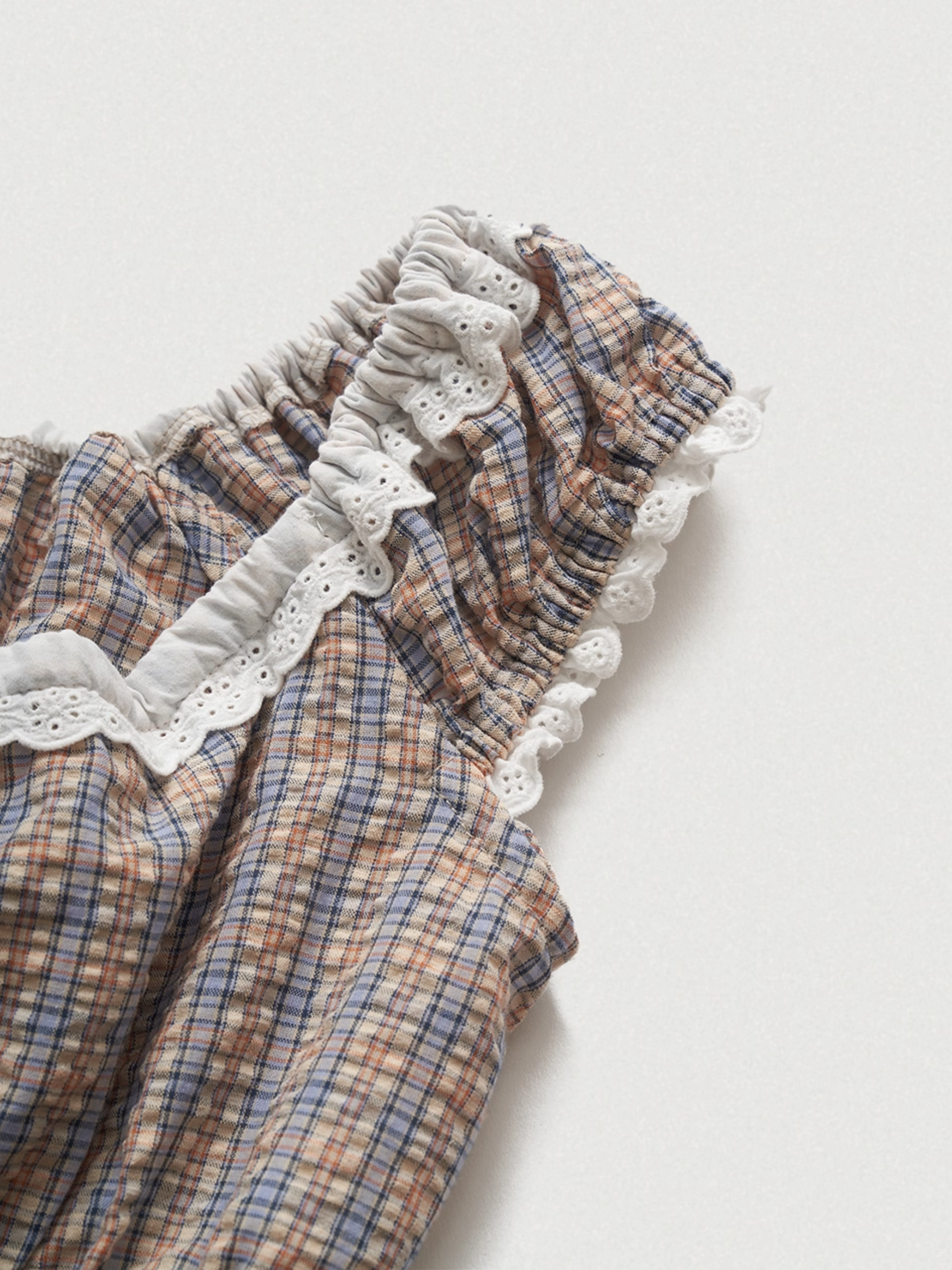 Plaid baby romper with ruffled lace details on a light background