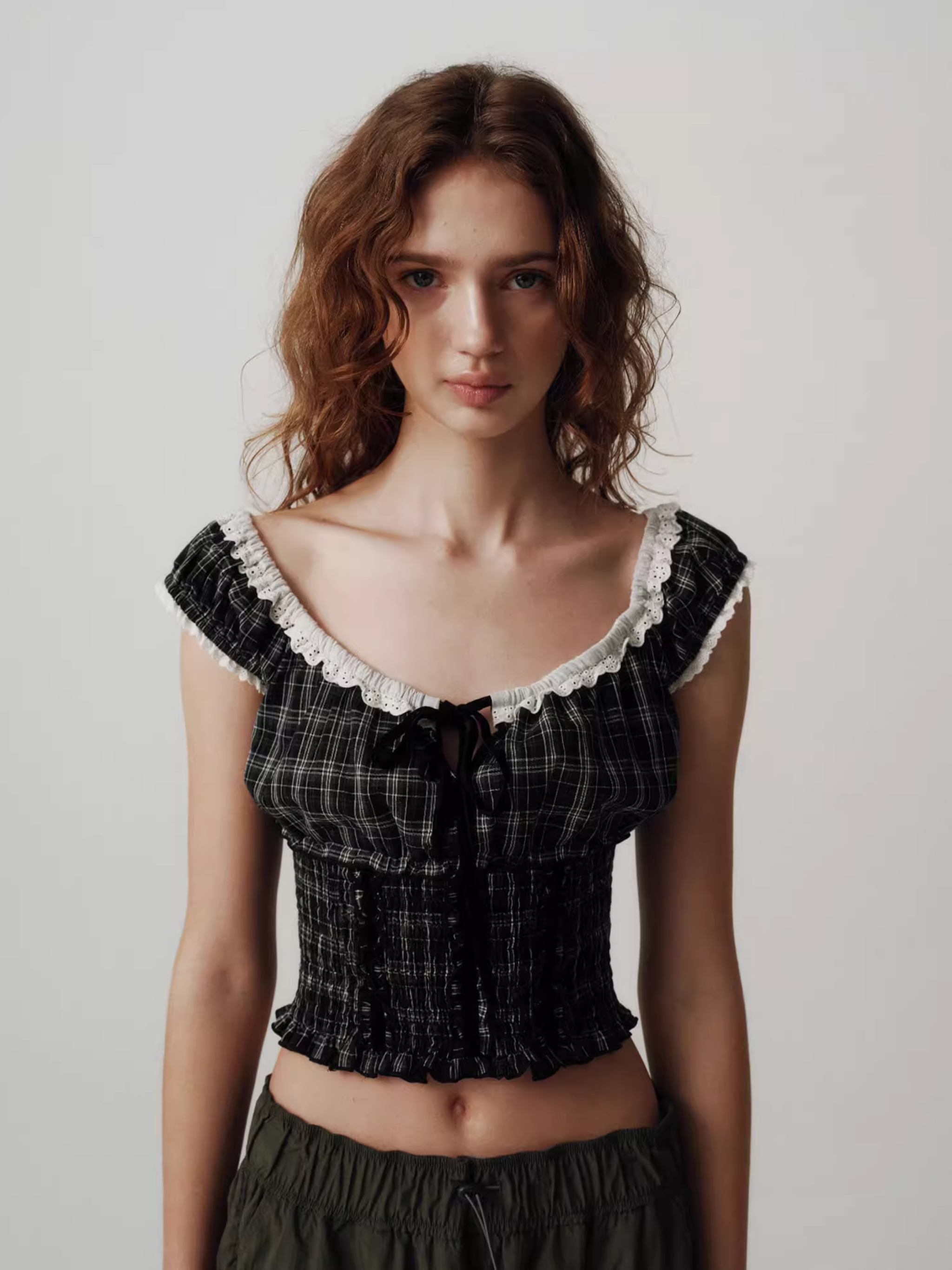 Woman wearing a black plaid top with white lace details on a plain background