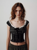 Woman wearing a black plaid top with white lace details on a plain background