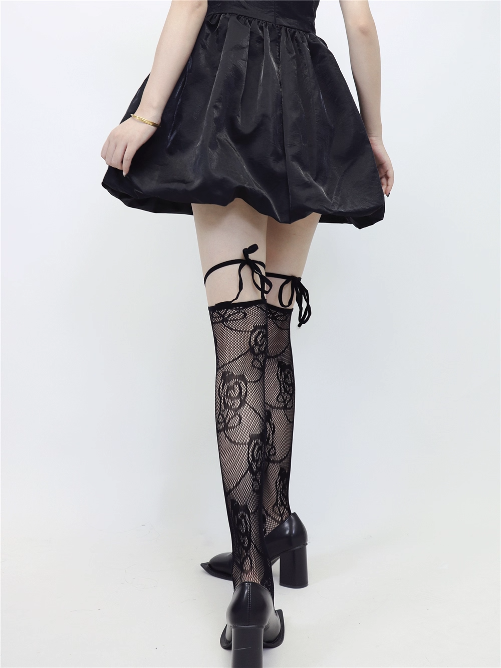 Person wearing a black skirt and black lace-up stockings on a white background