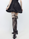 Person wearing a black skirt and black lace-up stockings on a white background