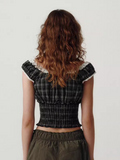 Person wearing a black plaid top with ruffled sleeves on a plain background