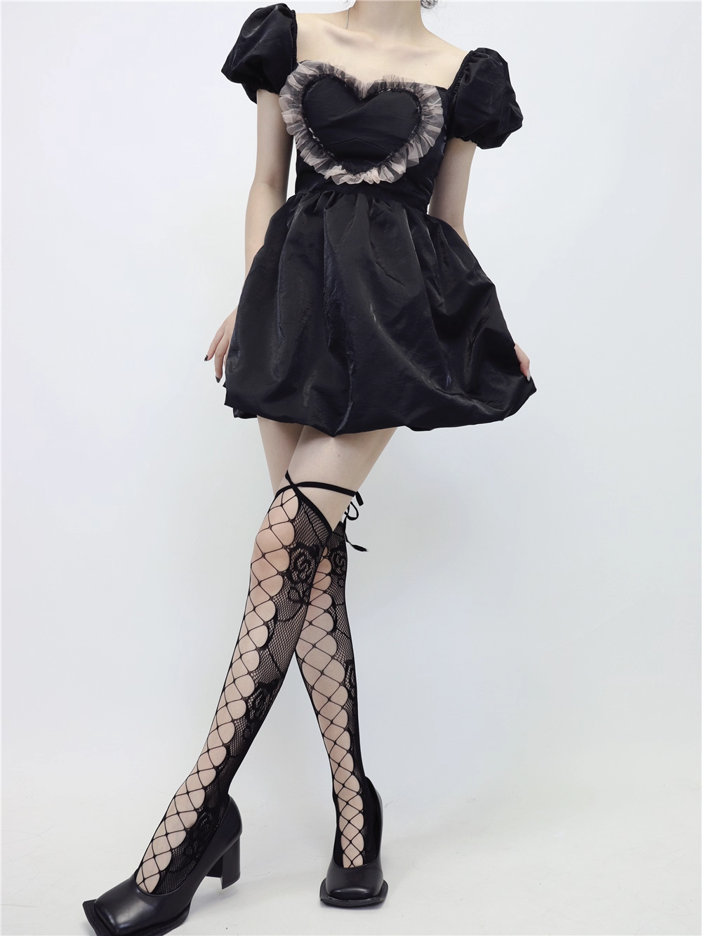 Black dress with heart-shaped neckline and fishnet stockings on a white background